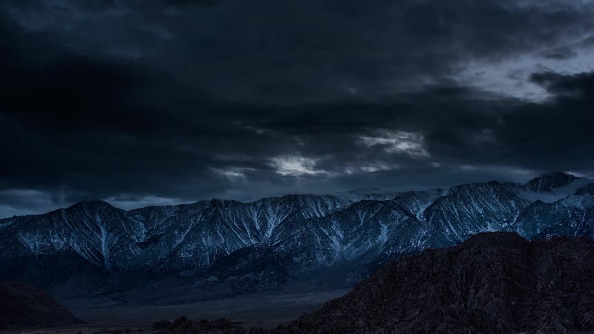 Storm clouds roll over snowy mountains as night falls