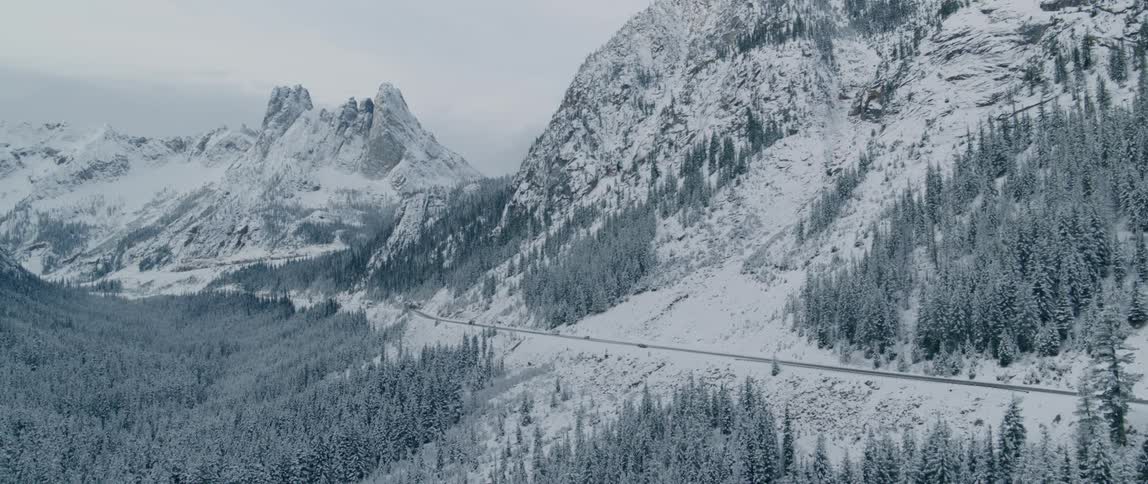 Road passes along snow and conifer forest covered mountains