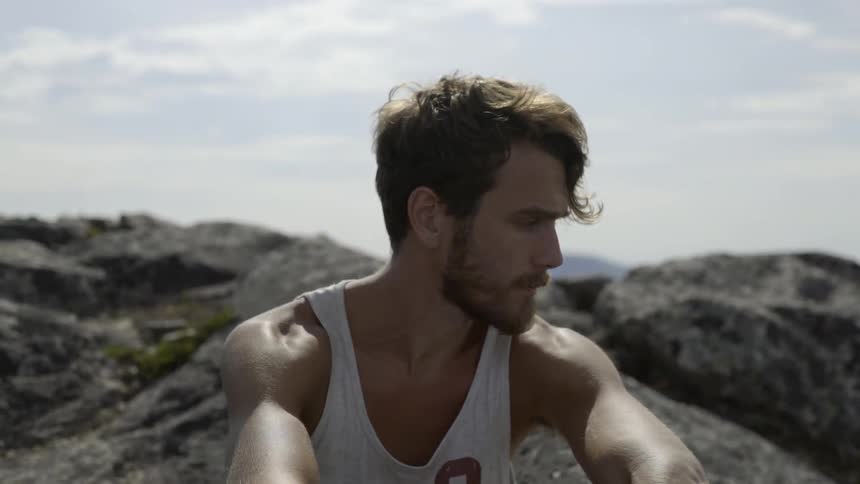 Active male hiker taking a break on a rugged mountain slope in the summer.
