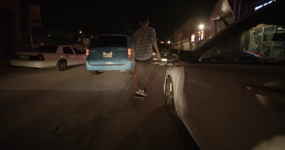 A young man skateboards between traffic on a city street at night