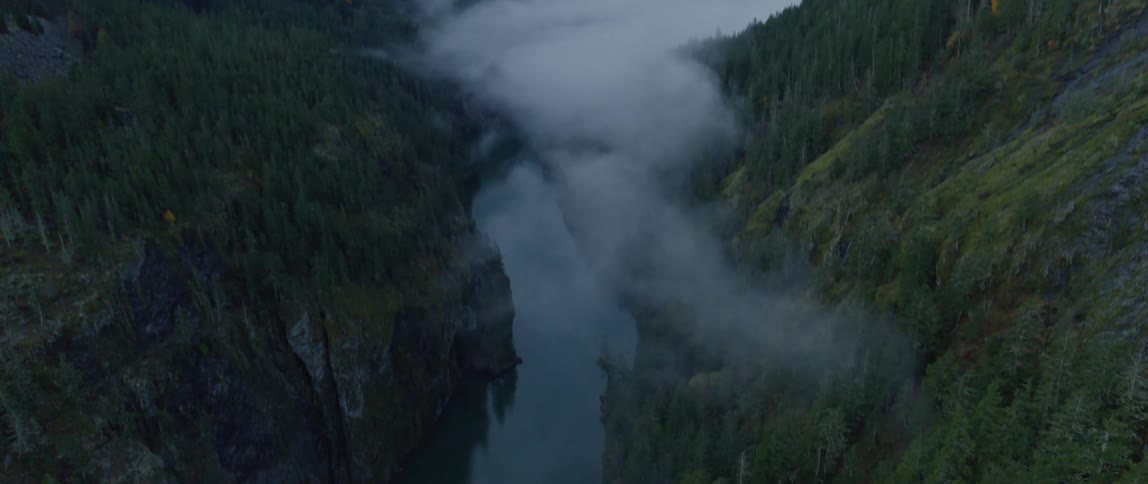 Thick fog sits above a river near snow capped mountains