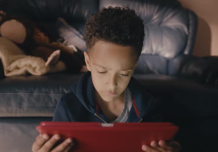 A young boy sits at home and looks at a tablet
