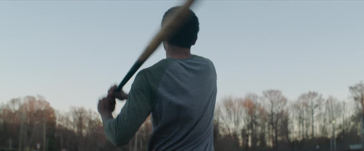 A man hits a ball with a bat during the day