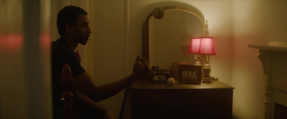 A man playing with a baseball as he sits on the edge of a bed