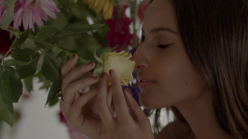 A woman smells a flower hanging from a vine