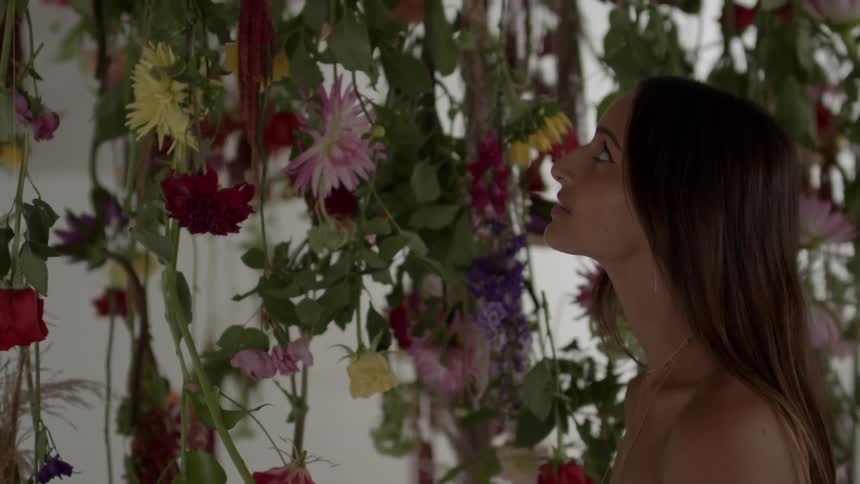A long haired woman looks up at some flowers