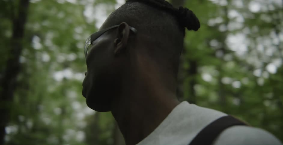 A black man wearing protective glasses is looking around in the woods