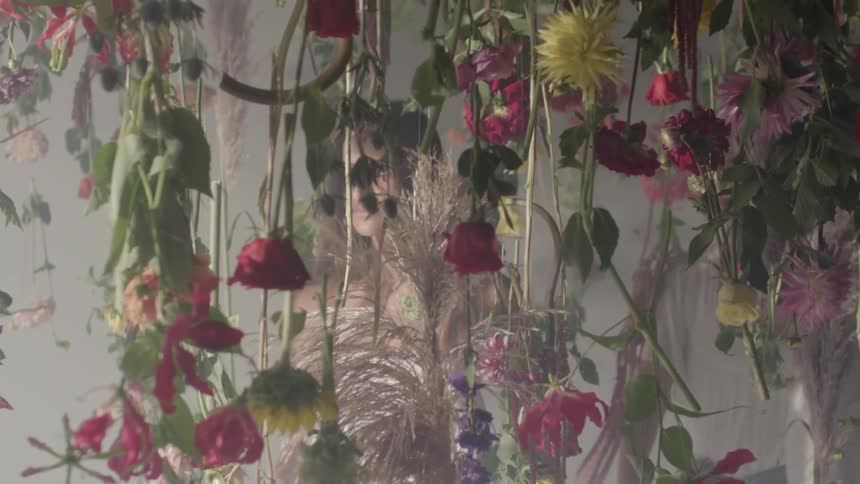 A woman walks through vines covered in flowers