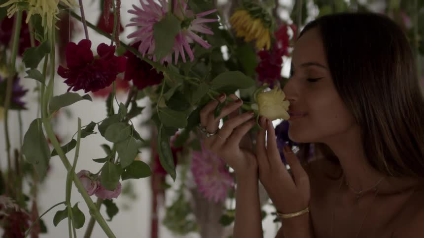 A woman smells a yellow rose which is hanging upside down