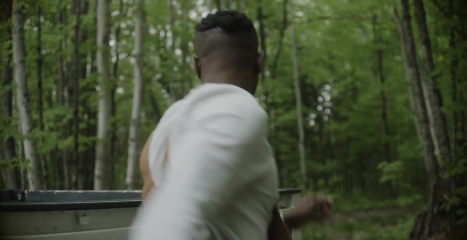 A man in a forest gets out of his truck and grabs a chainsaw and walks towards some trees