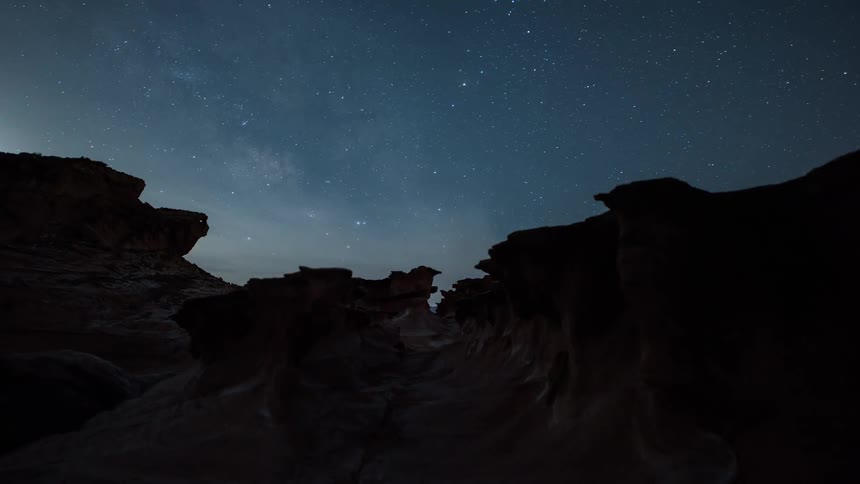 Stars shine brightly as they move over mountains and rock formations across the night sky