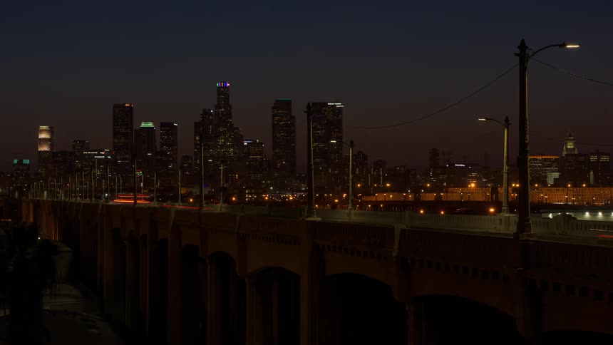 Car lights stream across a bridge with a city skyline behind