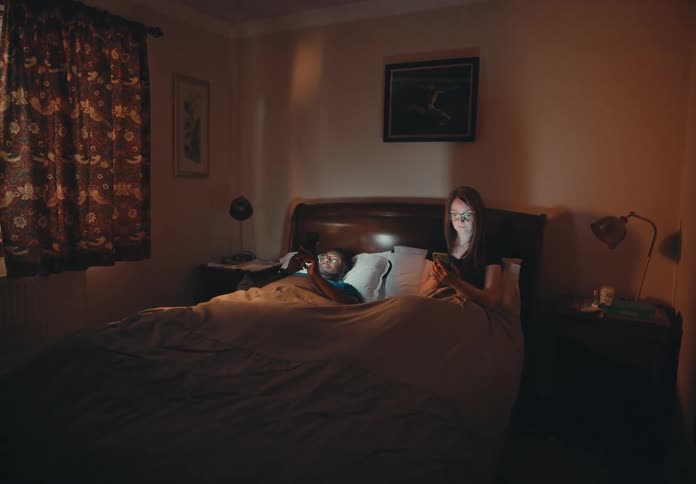 A man and woman are relaxing in bed as they play on their mobile phones