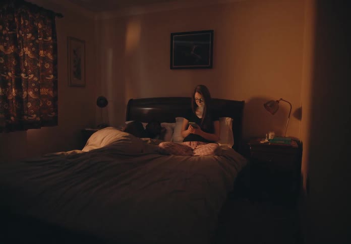 Woman sits up in bed with smartphone next to a sleeping man