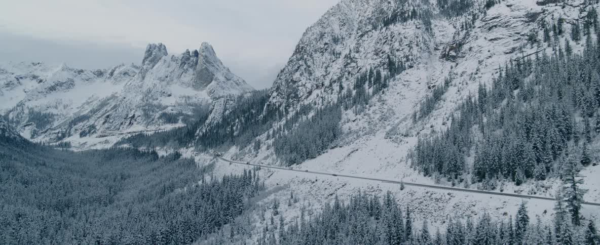 Vehicles travel on a road between snowy mountains