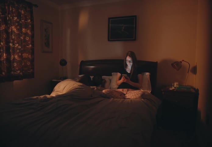 A woman sitting in bed using a smartphone while her husband sleeps