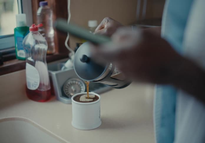 A man looks at his cell phone while pouring coffee from a french press and makes a mess