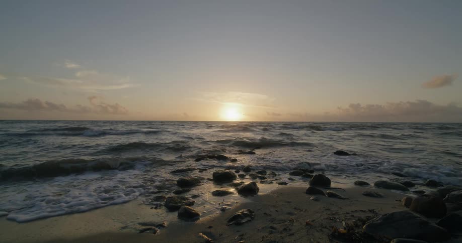 The sun is on the horizon as waves roll into a beach