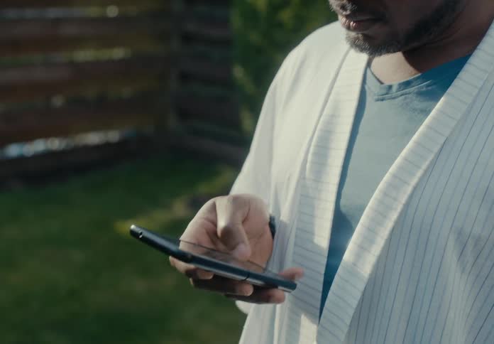 A man is standing outside looking at his phone as he scrolls with his thumb