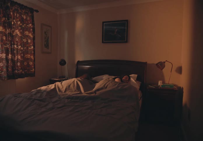 A timelapse of a man sitting in bed texting while his wife sleeps and then he lies down and sleeps and she sits up and texts