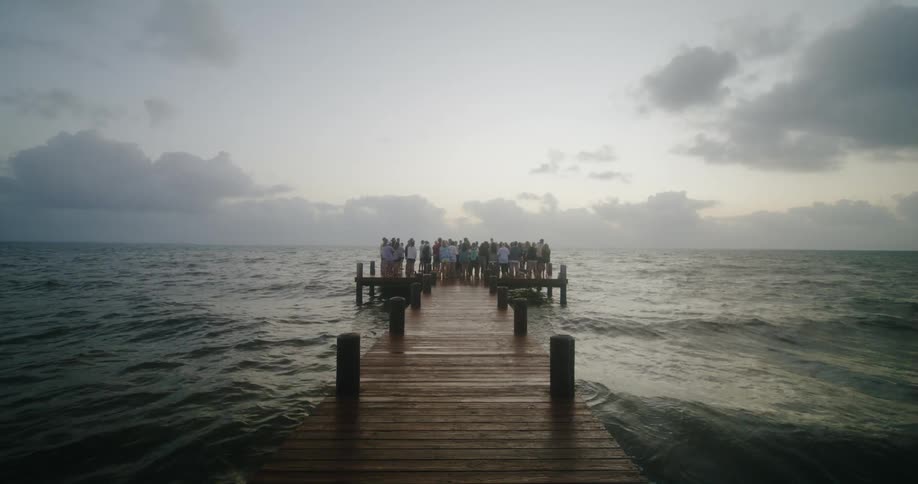 Crowd stands at end of pier as waves roll past