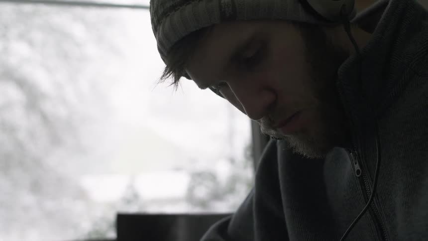 A man is leaning forward as it snows outside