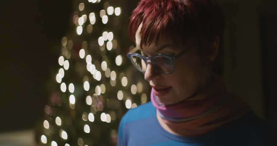 A woman stands near a christmas tree talking