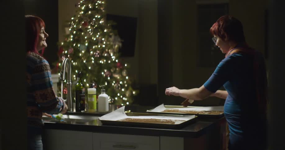 Two women smear chocolate frosting onto a baking sheet