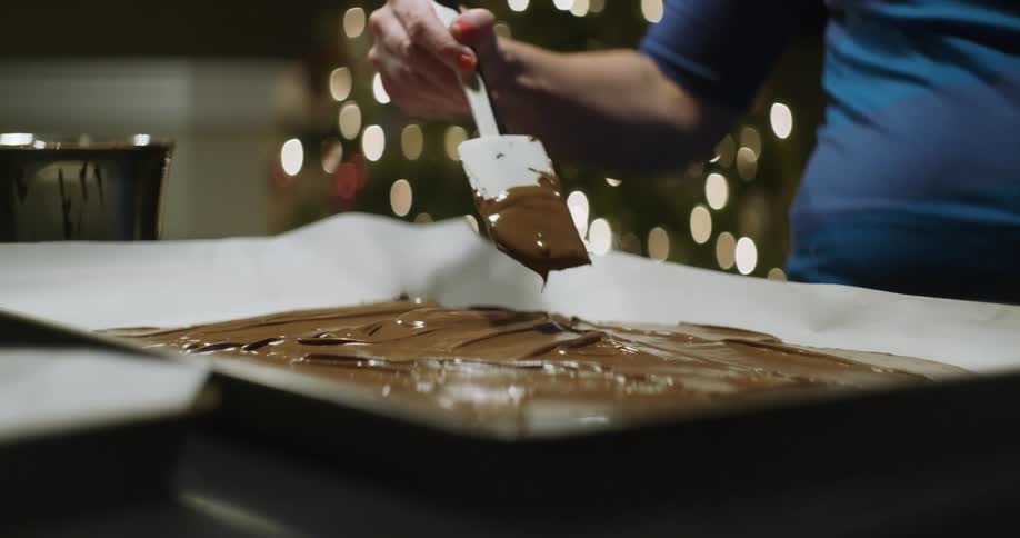 Woman smears chocolate frosting onto a baking sheet