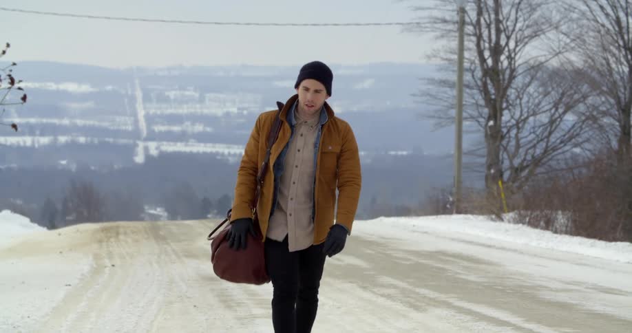 A man walks down a snowy country road in winter
