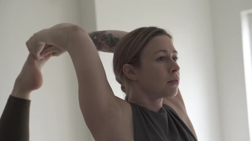A woman in dark clothes stretches in a white room