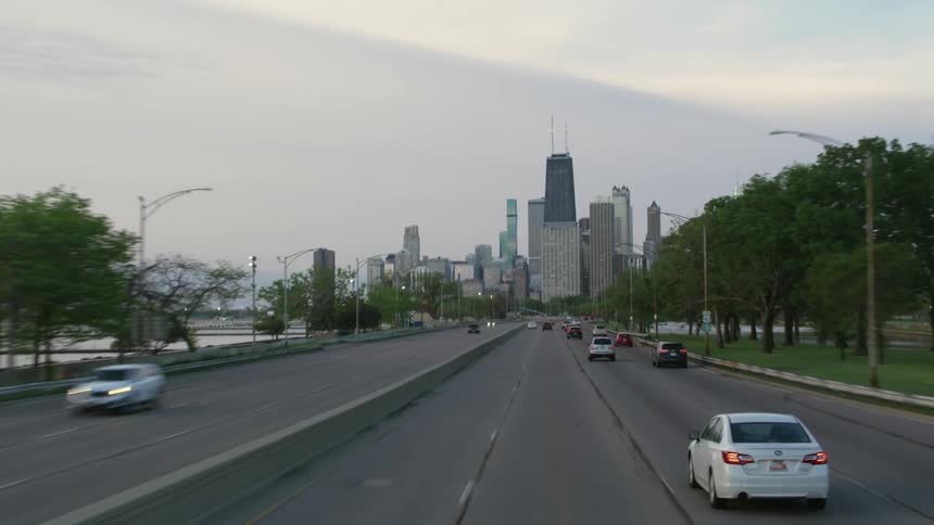 Vehicles drive along highway toward city downtown with water on both sides of roadway