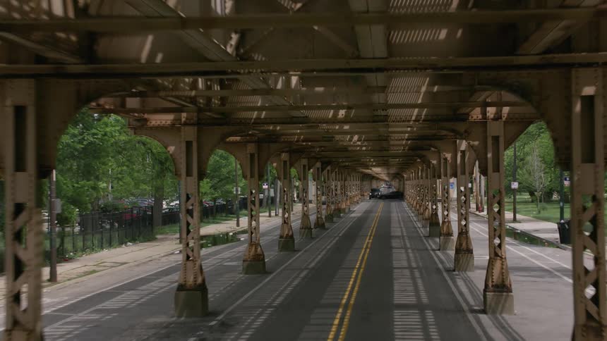 Cars traveling through an intersection and under elevated train tracks on a city street