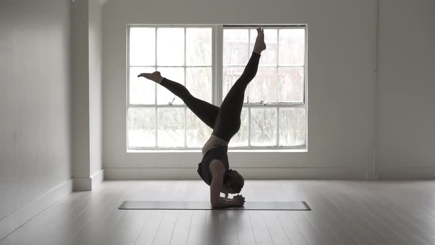 A woman does a handstand kicking her legs up slowly