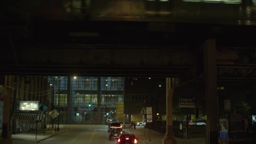 Vehicles drive through a neighborhood as a train passes by on elevated tracks