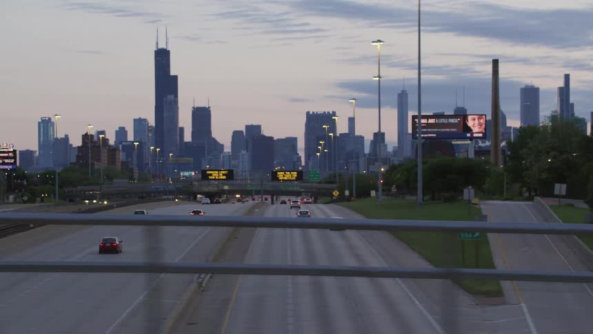A busy highway leads into a large city with several skyscrapers in the evening