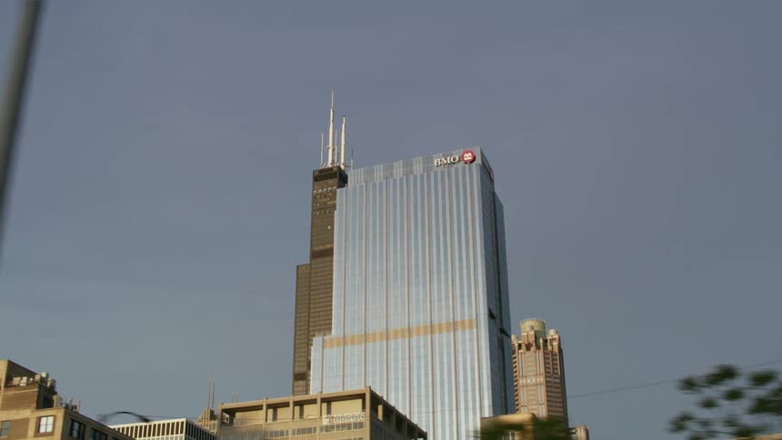 Glimpses of chicago towers are seen from beneath multiple overpasses on the highway