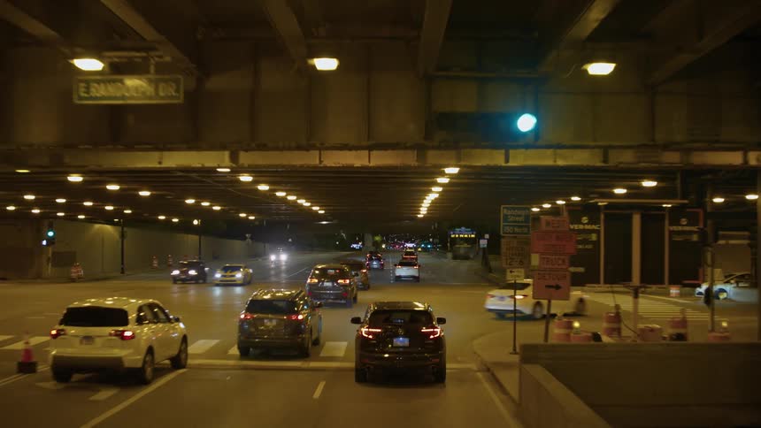 Cars traveling on wide city streets past intersections and underground public parking at night