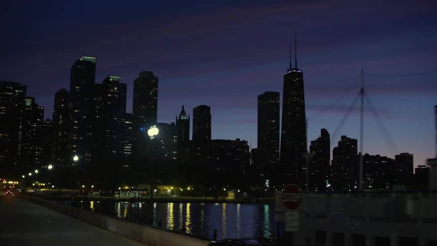 A boat sits docked at a bridge on the chicago river at night with the city in the background