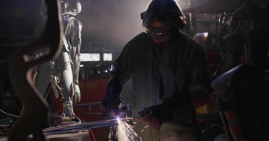 Sparks fly around a welder in a workshop