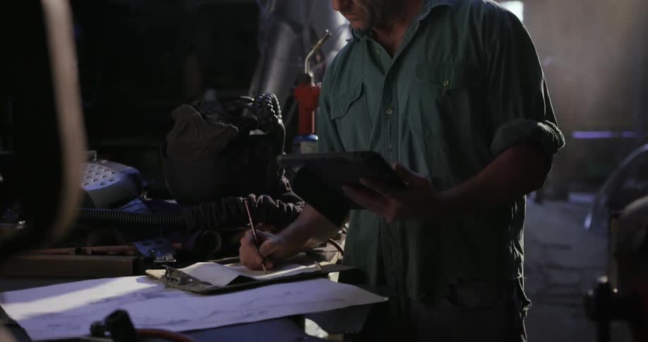 A man is writing down something on a clipboard in a garage