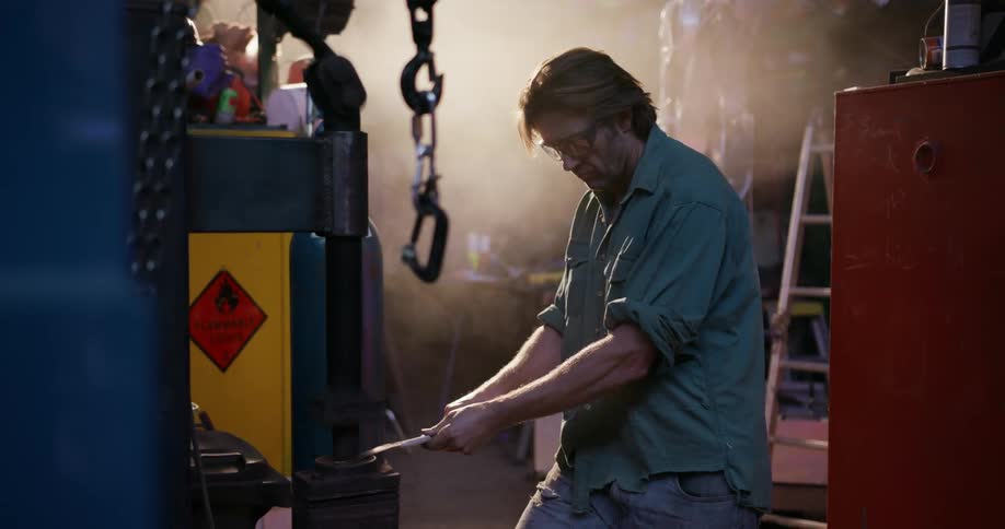 Man holds a piece of metal under a machine that pounds it flat