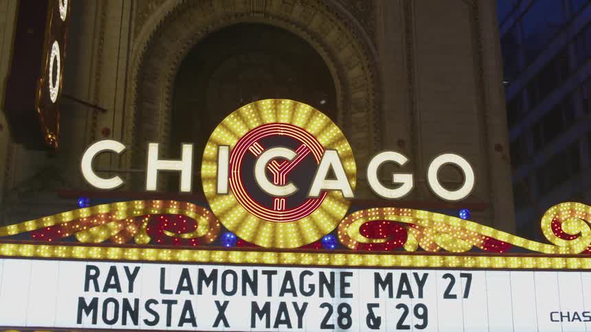 The chicago theater sign lights up a downtown street at night as automobiles pass by and people walk on the sidewalk