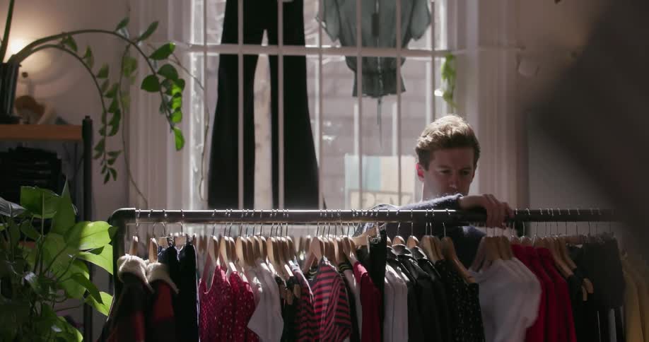A man arranges the clothes on a rack in a store