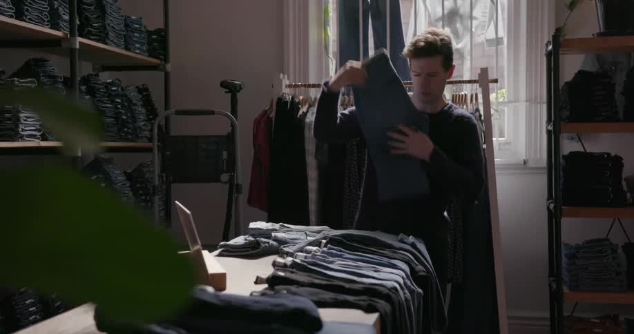 Man is folding jeans on table in clothing store