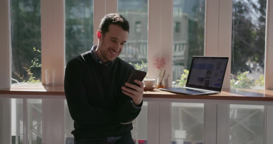 Man laughing as he looks at his cell phone inside building