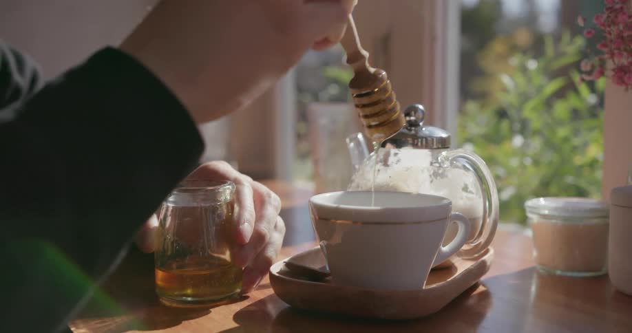 A person puts some honey in a teacup