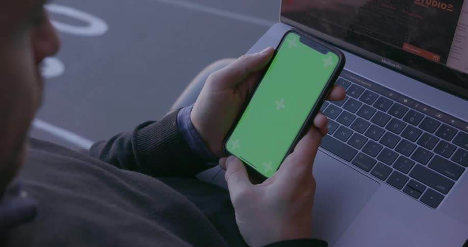 Man scrolls on his phone with a laptop on his lap