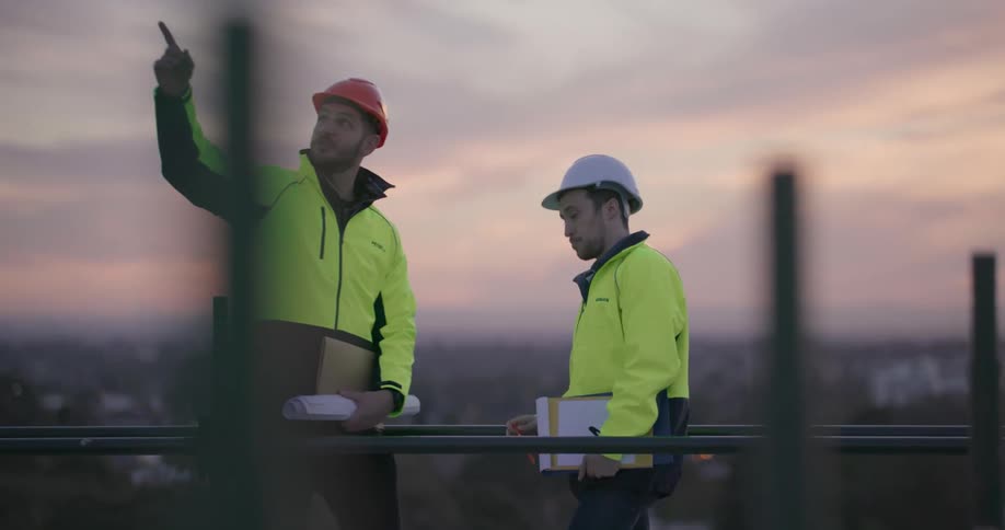 Two construction workers are discussing something on top of a building