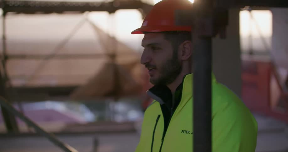 Two workers talk at a construction site at sunset